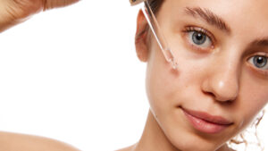 Close-up of woman applying hydrating serum to her face, emphasizing skincare and natural beauty care against a white studio background. Concept of fashion, appearance, self care. Ad